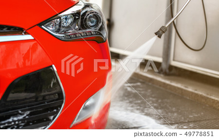 Front light of red car washed in self serve carwash, high pressure jet water stream spraying on 49778851