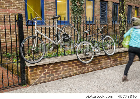 Old bicycles locked to metal fence, high above ground, blurred person passing by on pavement Old bicycles locked to metal fence, high above ground, blurred person passing by on pavement 49778880