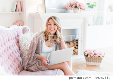 Portrait of gorgeous blonde woman with laptop working at home. Woman sitting on pink sofa in light 49787119