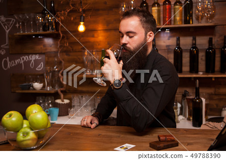Young tattooed bartender with great beard tasting a glass of wine. 49788390