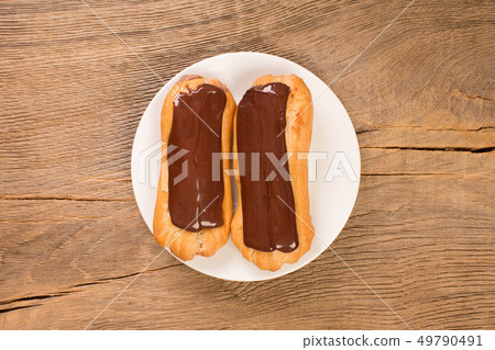Freshly baked chocolate eclairs on white plate, top view. 49790491