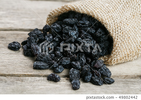 Black raisins in burlap bag over wooden gray table Black raisins in burlap bag over wooden gray table 49802442