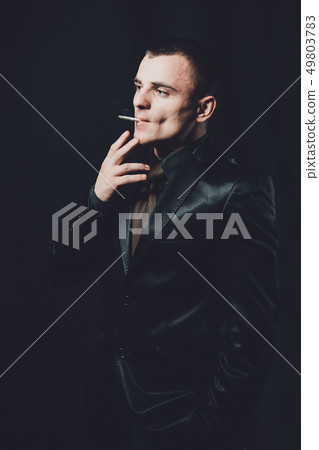 a young man smokes a cigarette, a black background, a classic black suit 49803783