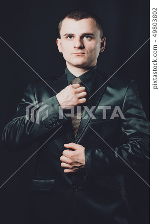 young stylish guy dressed in black classic suit on a black background 49803802
