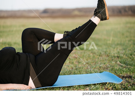 Overweight woman training legs on yoga mat outdoor Overweight woman training legs on yoga mat outdoor 49814301