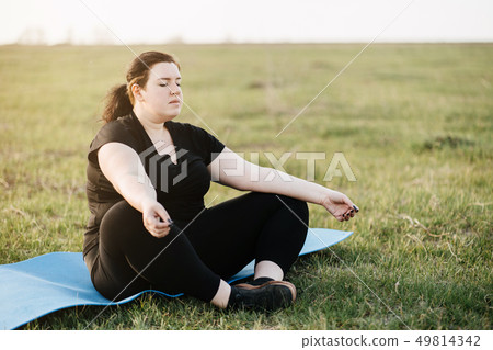 Overweight woman meditating at yoga mat outdoors Overweight woman meditating at yoga mat outdoors 49814342