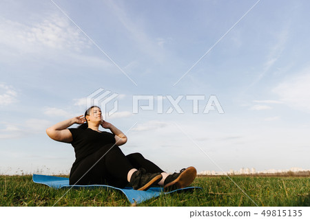 Overweight woman doing sit-ups outdoors. 49815135