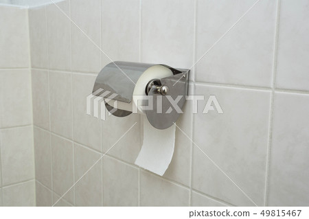 A white roll of soft toilet paper neatly hanging on a modern chrome holder on a light bathroom wall. 49815467