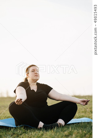 Overweight woman meditating at yoga mat outdoors Overweight woman meditating at yoga mat outdoors 49815493
