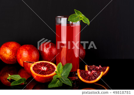 Glass of juice with a some pieces of sicilian orange on a black background. Sicilian orange drink. Glass of juice with a some pieces of sicilian orange on a black background. Sicilian orange drink. 49818781