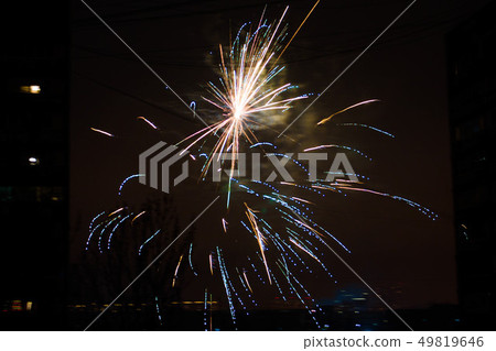 Night salute. Explosion lines of different colors. Outbreaks between houses. 49819646