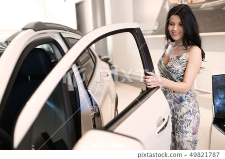 Beautiful fashionable brunet look at her new car in dealership showroom Beautiful fashionable brunet look at her new car in dealership showroom 49821787