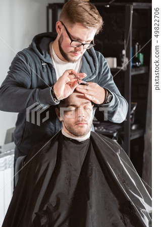 Hair cutting with metal scissors. Master cuts hair and beard of men in the barbershop, hairdresser 49822706