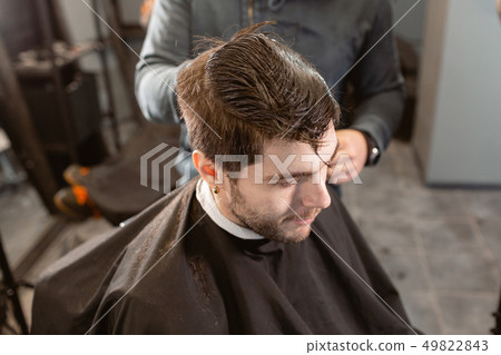 Master cuts hair and beard of men in the barbershop, hairdresser makes hairstyle for a young man 49822843