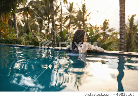 Woman in white swimsuit in outdoor pool on green jungle background 49825165