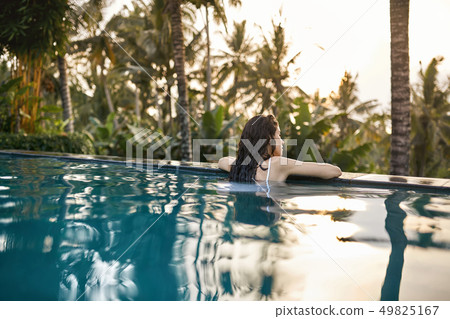 Woman in white swimsuit in outdoor pool on green jungle background 49825167