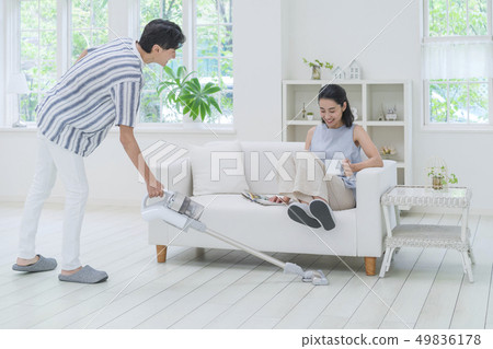A man vacuuming and a woman sitting on a couch and raising both legs 49836178