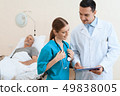 man lies on a cot. Doctor and a nurse help him. 49838005