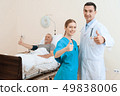 man lies on a cot. Doctor and a nurse help him. 49838006