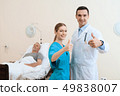 man lies on a cot. Doctor and a nurse help him. 49838007