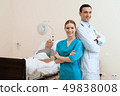 man lies on a cot. Doctor and a nurse help him. 49838008