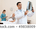 man lies on a cot. Doctor and a nurse help him. 49838009