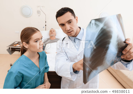 man lies on a cot. Doctor and a nurse help him. 49838011