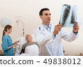 man lies on a cot. Doctor and a nurse help him. 49838012