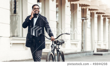 African-american businessman talking on phone, riding bicycle African-american businessman talking on phone, riding bicycle 49844208
