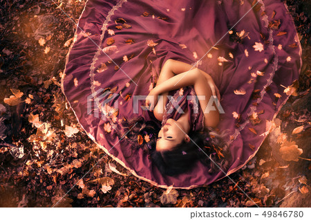 Young attractive woman in purple dress lying in the middle of autumn leaves. Young attractive woman in purple dress lying in the middle of autumn leaves. 49846780