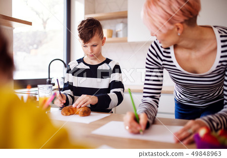 A young woman with two children drawing in a kitchen. A young woman with two children drawing in a kitchen. 49848963