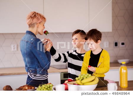 A young woman with two children eating fruit in a kitchen. A young woman with two children eating fruit in a kitchen. 49848964