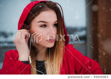 A close-up portrait of young girl or woman with earphones outdoors, listening to music. A close-up portrait of young girl or woman with earphones outdoors, listening to music. 49848965