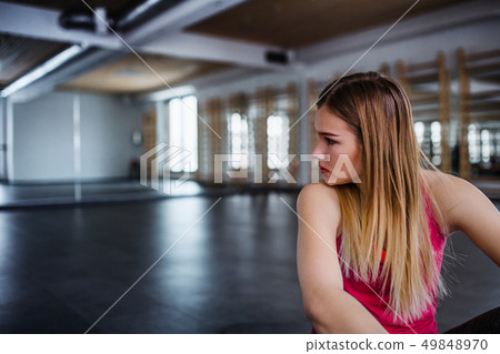 A portrait of young sad and frustrated girl or woman sitting in a gym. 49848970