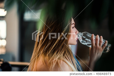 A side view of young girl or woman standing in a gym, drinking water. A side view of young girl or woman standing in a gym, drinking water. 49848973