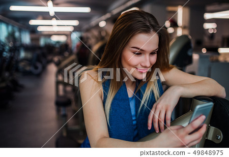 A portrait of young girl or woman with smartphone in a gym, taking selfie. A portrait of young girl or woman with smartphone in a gym, taking selfie. 49848975