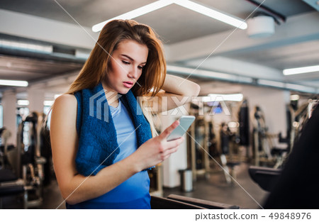 A portrait of young girl or woman with smartphone in a gym. A portrait of young girl or woman with smartphone in a gym. 49848976