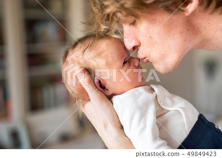 A young father holding a newborn baby at home, kissing him. A young father holding a newborn baby at home, kissing him. 49849423