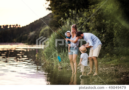 A young family with two toddler children outdoors by the river in summer. 49849479
