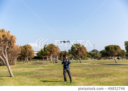 A man piloting a drone in the park in spring-summer time A man piloting a drone in the park in spring-summer time 49852746