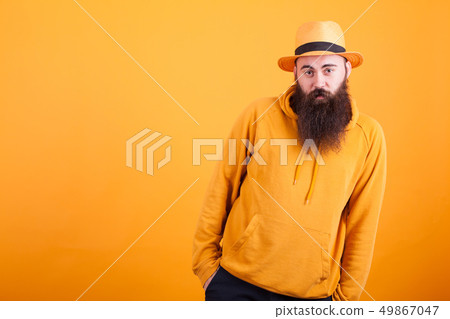Cool bearded hipster with orange hat holding hands in his pockets over yellow background Cool bearded hipster with orange hat holding hands in his pockets over yellow background 49867047