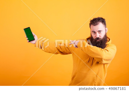 Bearded hipster in yellow hoodie pointing at phone over yellow background Bearded hipster in yellow hoodie pointing at phone over yellow background 49867181