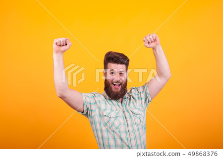 Portrait of happy bearded man with fists up celebratin over yellow background 49868376