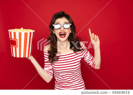 Happy brunette lady with box of pop corn on red 49869658