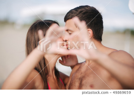 Happy young couple kiss and make a heart by hands. Couple walking on the beach. Love Happy young couple kiss and make a heart by hands. Couple walking on the beach. Love 49869659