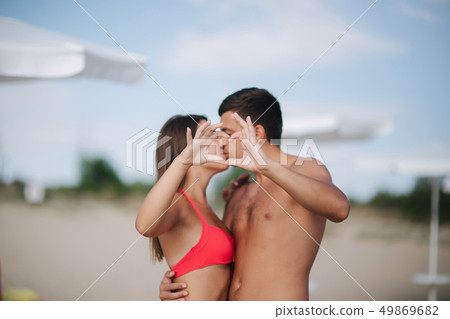 Happy couple make a heart. Woman and man on the beach. They kiss Happy couple make a heart. Woman and man on the beach. They kiss 49869682
