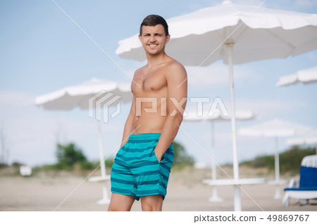 Man in shorts stand on the beach. Sun shines into his eyes and he squint 49869767