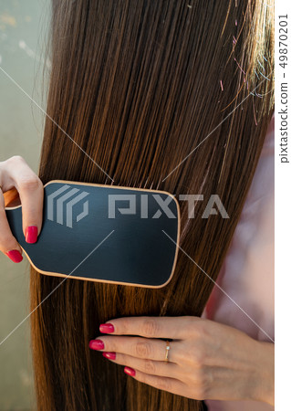 Brunette girl in a pink shirt is combing her beautiful long hair comb 49870201