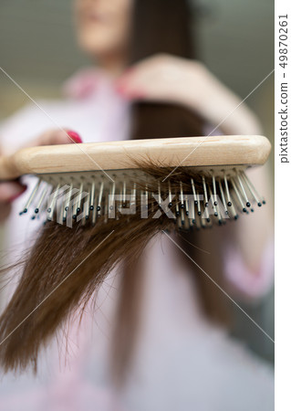 Brunette girl in a pink shirt is combing her beautiful long hair comb 49870261