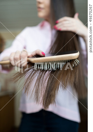 Brunette girl in a pink shirt is combing her beautiful long hair comb 49870267